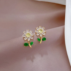 Macro shot of gold daisy flower stud earrings with green leaf crystals on pink silk