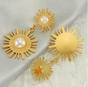 Détail de boucles d'oreilles soleil dorées vintage avec perles sur fond de soie