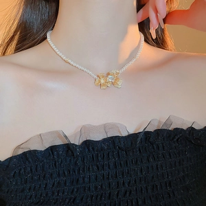 Close-up of pearl necklace featuring a golden floral pendant with a clear zircon stone