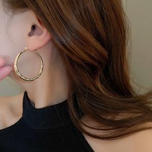 Close-up of textured golden hoop earrings with woven pattern on woman's ear