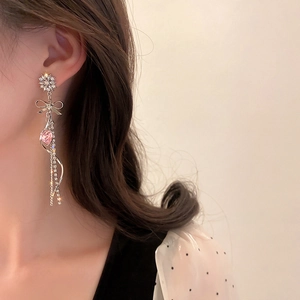Detail of silver long tassel earring with pink heart gemstone and bow design on model