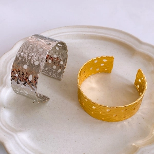 Detalle de brazaletes anchos en oro y plata con textura martillada y huecos circulares