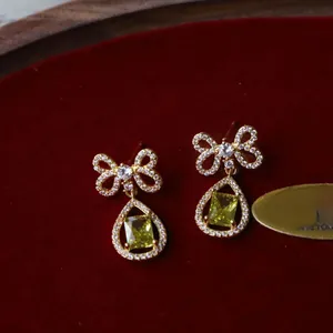 Macro shot of bowknot earrings with yellow rectangle stones on red velvet background
