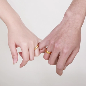 Close-up of a couple holding pinky fingers wearing gold stainless steel beveled rings