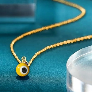 Detailed close-up of yellow evil eye pendant with blue eye on gold beaded chain
