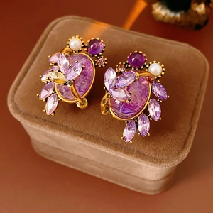 Macro detail of vintage gold stud earrings with purple crystals and a white pearl accent