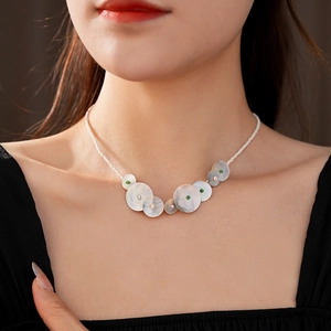 Detail of round shell necklace with white beads and green accents on female model