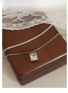 Detail of silver double layered chain necklace with a zircon pendant on a wooden box