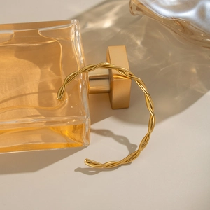 Minimalist twisted 18K gold plated stainless steel open bangle on a glass perfume bottle