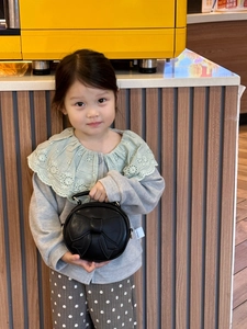 Close-up of kids black round handbag with bow detailing held by a young child