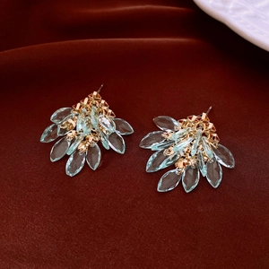 Close-up of light blue crystal leaf-shaped cluster earrings on a red velvet background