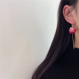 Close-up of pink dried rosebud earrings with elegant long gold tassel chain on a model