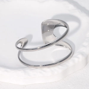 Macro view of minimalist silver streamline bangle on white textured tray with metallic finish