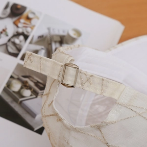 Close-up of beige baseball cap featuring metallic lattice embroidery and adjustable strap