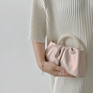 Detail of champagne satin pleated handbag featuring a luxury pearl beaded handle