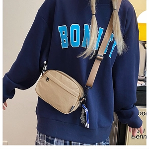 Gros plan d'un sac bandoulière en nylon kaki avec large sangle porté par un mannequin