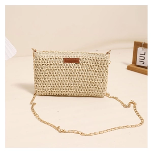 Detail of khaki straw crossbody bag featuring woven texture and gold metal chain strap