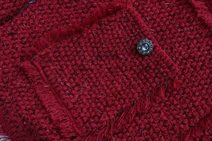 Détail macro d'une veste en tweed rouge foncé avec fils métalliques et bouton diamanté