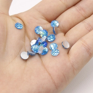 Macro shot of 6mm blue fish scale resin cabochons held in palm for scale and detail