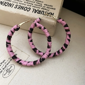 Gros plan détaillé des boucles d'oreilles créoles tissées léopard rose et noir sur livres