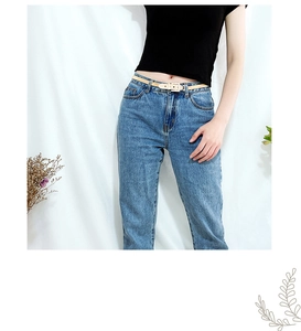 Detail view of a beige elastic spring metal waist belt paired with blue denim jeans