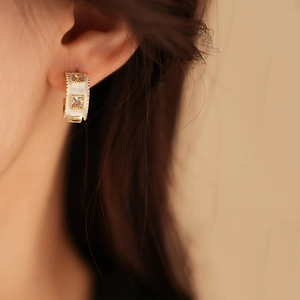 Detail of C-shaped gold plated earring with white inlay and crystal on model's ear