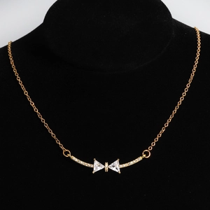 Detail of gold-plated bow necklace with white zircon stones on a black display stand