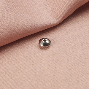 Dettaglio macro di una perla distanziatrice piatta in acciaio inox su tessuto rosa