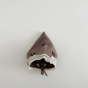 Detailed close-up of brown knit baby bonnet featuring white lace trim and bow accents