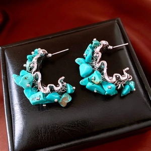 Detail of C-shaped silver earrings with turquoise stones on black leather pad