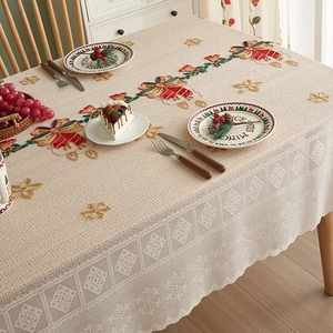 Close-up of beige Christmas tablecloth with red bell embroidery and delicate lace edges