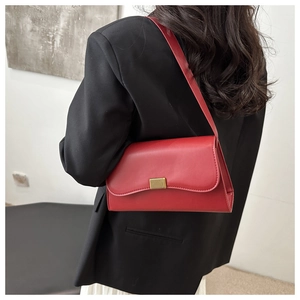 Close-up of a red leather baguette shoulder bag with gold buckle on black blazer
