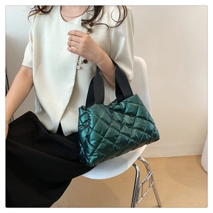 Detail of dark green quilted metallic tote bag featuring diamond stitch and black straps