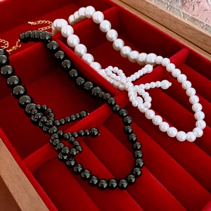 Elegant faux pearl and black beaded necklaces with bow accents on a red velvet jewelry box