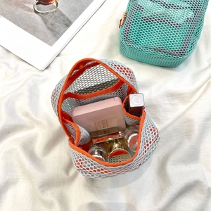 Macro view of a grey mesh mini makeup bag with vibrant orange trim and interior storage space
