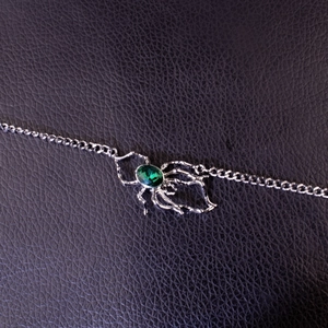 Macro shot of silver spider pendant featuring a faceted emerald green gemstone on a chain