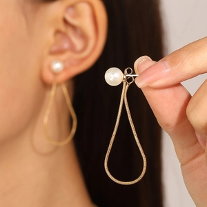 Detail of elegant gold teardrop earrings with pearl accents and snake chain links