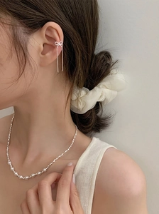 Detail of silver bow ear cuff with long tassels and a gradient pearl necklace on a model
