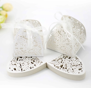 Detail of white laser-cut wedding favor box with rose patterns and silk ribbon bow