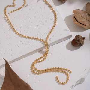 Minimalist gold beaded tassel necklace on a textured white stone and autumn leaves background