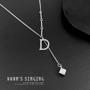 Macro shot of silver letter D necklace with small cube charm on a textured surface