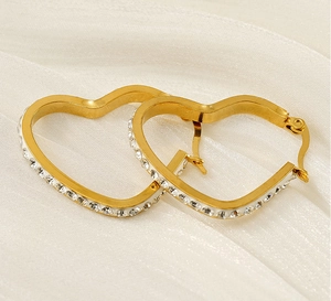 Macro view of 18k gold plated heart earrings with sparkling crystals on white silk