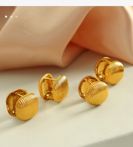 Gros plan de boucles d'oreilles créoles dorées rayées sur fond de tissu beige