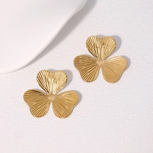 Minimalist gold clover flower earrings in stainless steel on white textured background