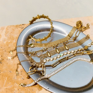 Detailed view of various gold-plated stainless steel bracelets and zircon jewelry on marble