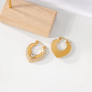 Detail view of heart-shaped gold earrings with pearl and crystal inlay on a white surface