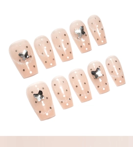 Macro view of nude cat-eye press-on nails with polka dots and silver 3D butterflies