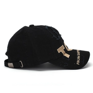 Detail of black baseball cap featuring gold letter T embroidery and distressed torn fabric