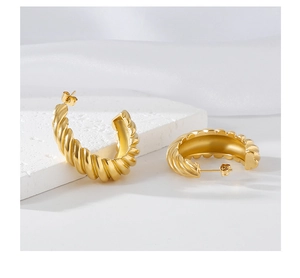 Detail of golden C-shape earrings with spiral texture on a soft silk background