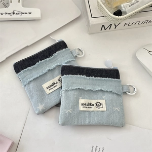 Detail der Denim-Münztasche mit Fransen und Clip auf einem weißen Schreibtisch
